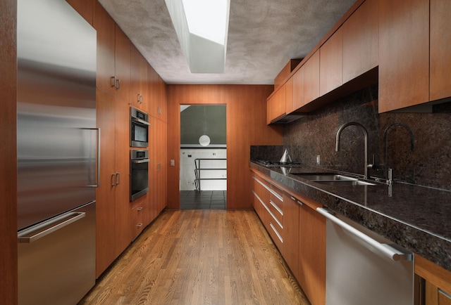 1944 Eucalyptus Hill Rd, Santa Barbara, CA 93108 - kitchen with appliances with stainless steel finishes, light wood finished floors, tasteful backsplash, brown cabinetry, and dark stone countertops