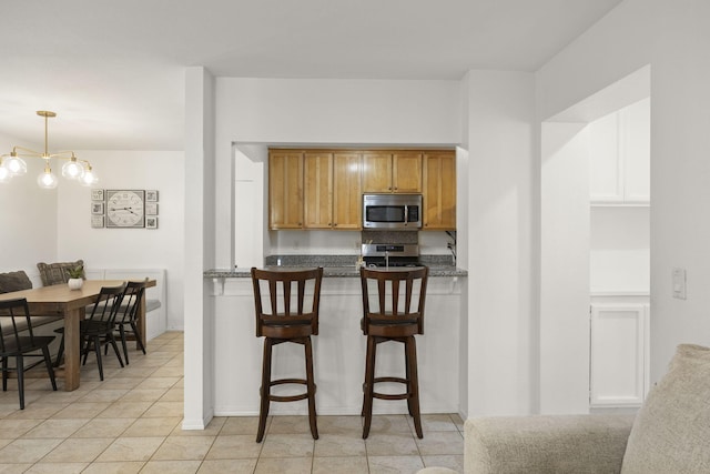 2171 Martinique Ln, Oxnard, CA 93035 - kitchen featuring appliances with stainless steel finishes, a kitchen bar, brown cabinets, light tile patterned flooring, and decorative light fixtures