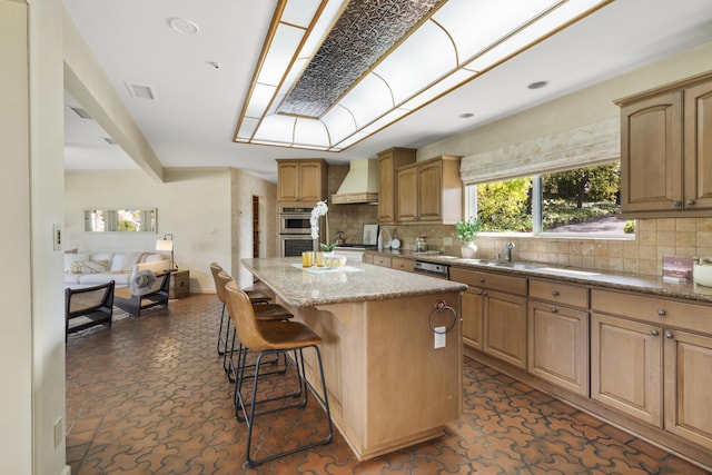 230 Avocado Pl, Camarillo, CA 93010 - kitchen featuring custom exhaust hood, a center island, a kitchen breakfast bar, light stone countertops, and decorative backsplash