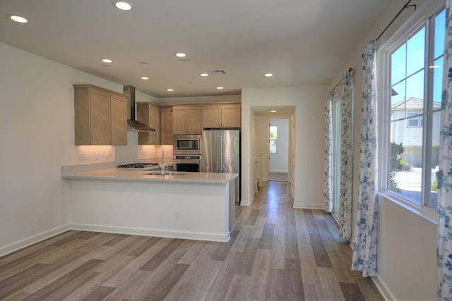 6628 Sand Castle Pl Unit C-7, Goleta, CA 93117 - kitchen with wall chimney exhaust hood, stainless steel appliances, light wood-style flooring, a peninsula, and light countertops