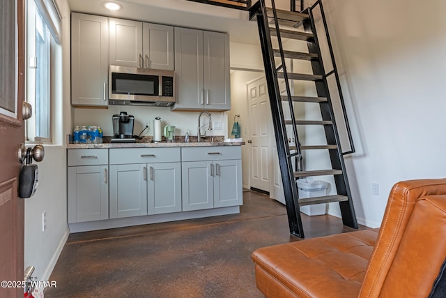 kitchen featuring baseboards, stainless steel microwave, light stone counters, and gray cabinetry