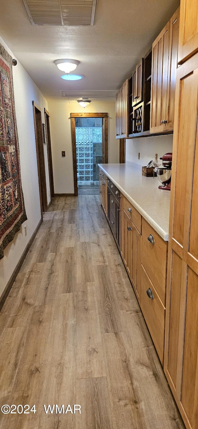 kitchen with brown cabinets, visible vents, light countertops, light wood-style flooring, and a textured ceiling