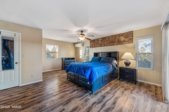 bedroom with wood finished floors, baseboards, ceiling fan, and a wall unit AC
