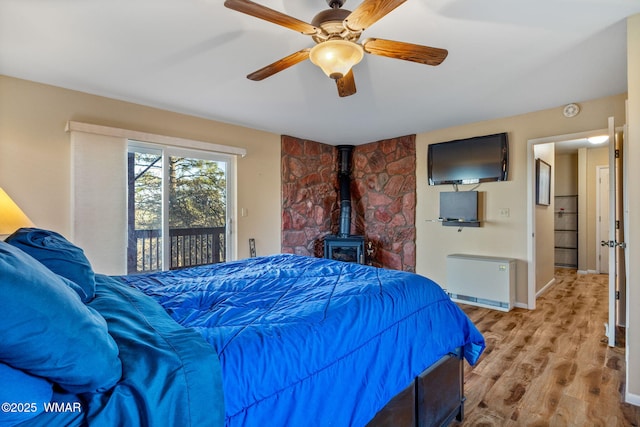 bedroom featuring a wood stove, radiator, baseboards, access to outside, and light wood-type flooring