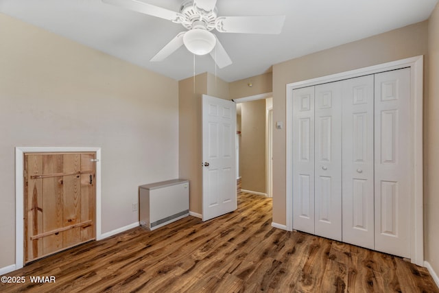 unfurnished bedroom with a closet, wood finished floors, refrigerator, baseboards, and a ceiling fan