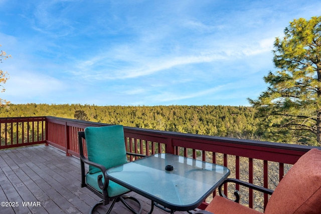 deck with outdoor dining area and a forest view