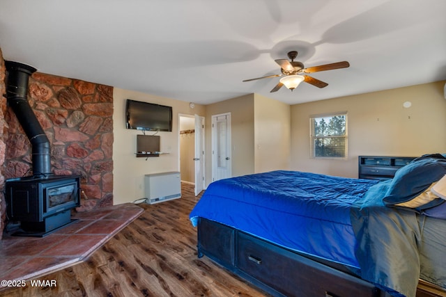 bedroom featuring a ceiling fan, a wood stove, and wood finished floors