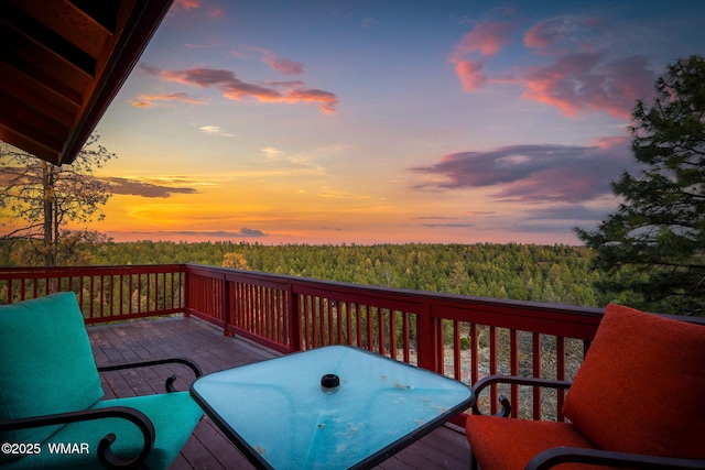 deck at dusk featuring a view of trees and outdoor dining area