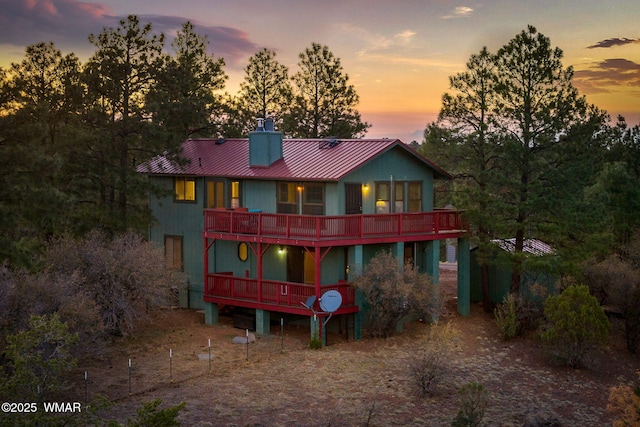back of house with a deck, a standing seam roof, metal roof, and a chimney