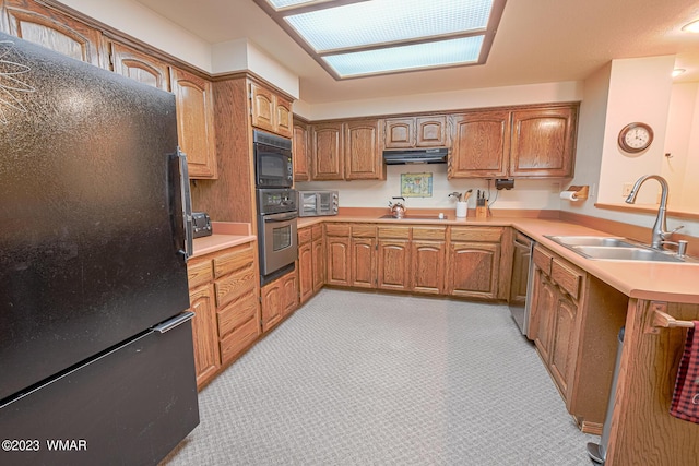 kitchen featuring light countertops, brown cabinetry, a sink, under cabinet range hood, and black appliances