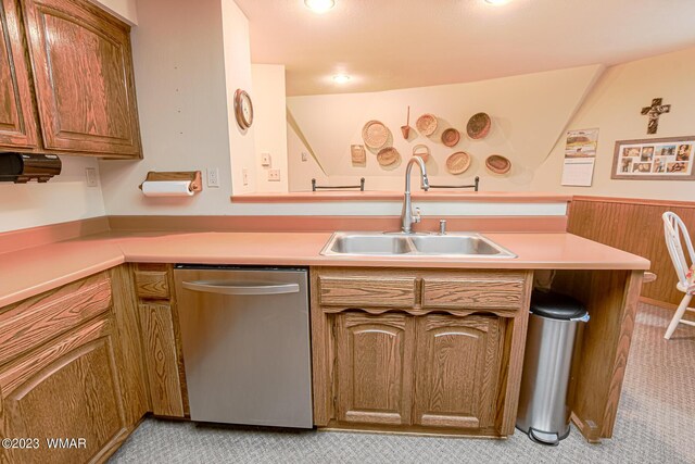 kitchen with brown cabinets, stainless steel dishwasher, light countertops, and a sink