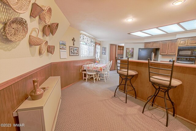 kitchen with black microwave, a breakfast bar area, light countertops, wainscoting, and freestanding refrigerator