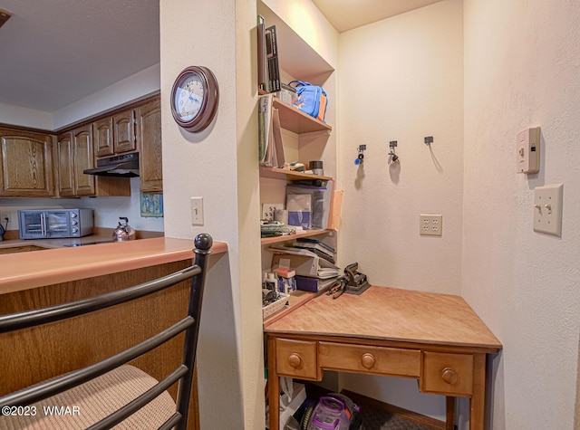 kitchen with a toaster, a textured wall, under cabinet range hood, and dark brown cabinets