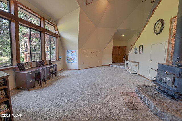 living room with high vaulted ceiling, a wood stove, light carpet, and baseboards