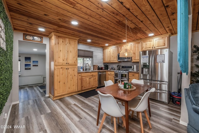 kitchen with stainless steel appliances, a sink, light wood-style floors, light brown cabinetry, and decorative light fixtures