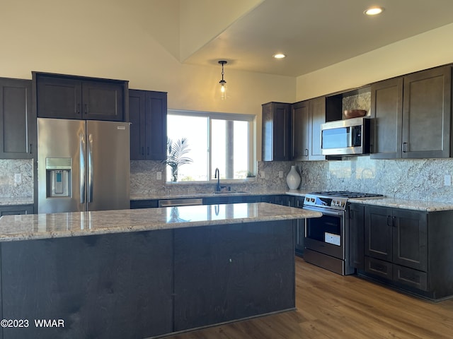 kitchen with light stone countertops, pendant lighting, stainless steel appliances, and a sink