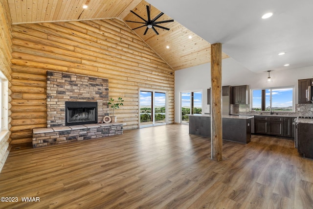 unfurnished living room featuring dark wood finished floors, a stone fireplace, high vaulted ceiling, a sink, and recessed lighting