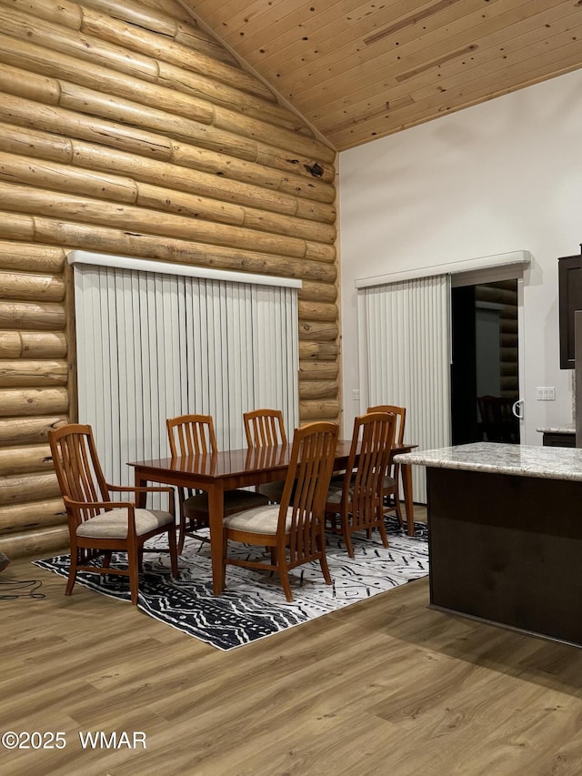 dining space featuring high vaulted ceiling, wooden ceiling, rustic walls, and wood finished floors