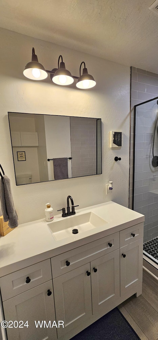 full bath featuring a textured ceiling, a textured wall, visible vents, vanity, and a shower stall