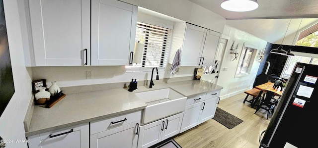 kitchen with light wood-style flooring, freestanding refrigerator, light countertops, white cabinetry, and a sink