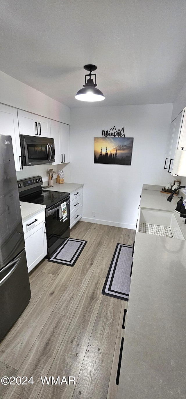 kitchen featuring a sink, white cabinets, light countertops, black appliances, and light wood finished floors