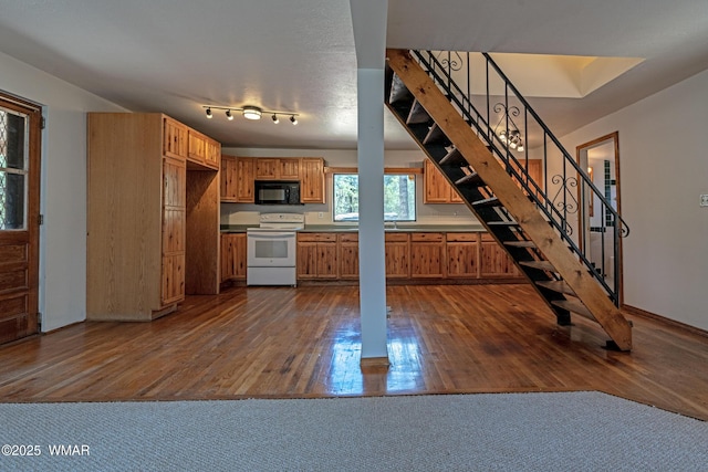 kitchen featuring electric stove, black microwave, dark wood-type flooring, brown cabinetry, and baseboards