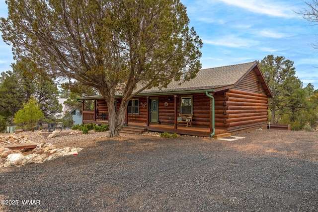 cabin with covered porch, log exterior, and roof with shingles