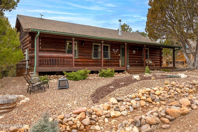 log-style house with a shingled roof, covered porch, and log siding