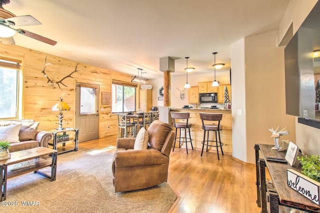 living area with wooden walls, a ceiling fan, and light wood-type flooring