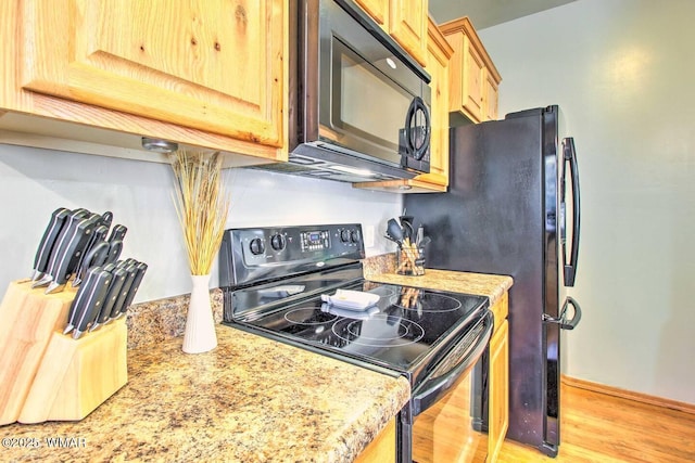 kitchen with light brown cabinets, black appliances, light wood-type flooring, and light stone countertops