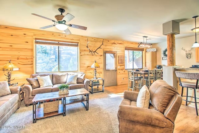 living area with light wood-type flooring, wood walls, and a ceiling fan