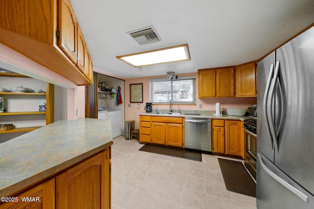 kitchen featuring visible vents, brown cabinets, a sink, appliances with stainless steel finishes, and independent washer and dryer