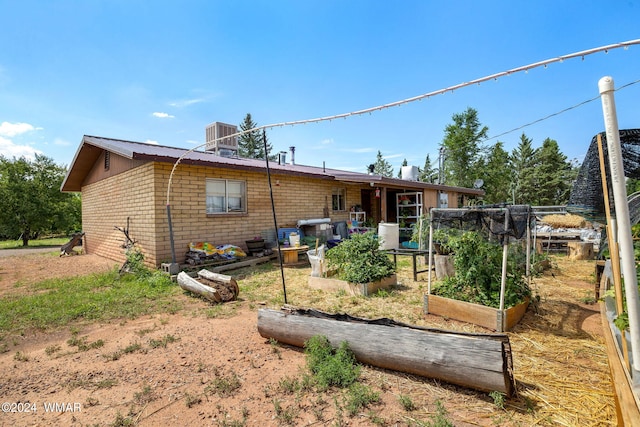 rear view of property with cooling unit, metal roof, a garden, and brick siding