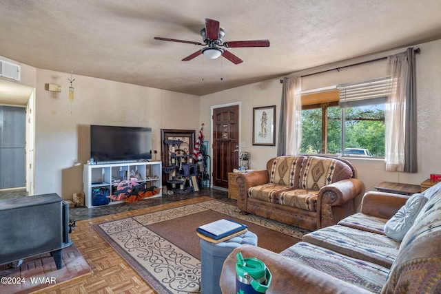 living room featuring a ceiling fan, a wood stove, visible vents, and a textured ceiling