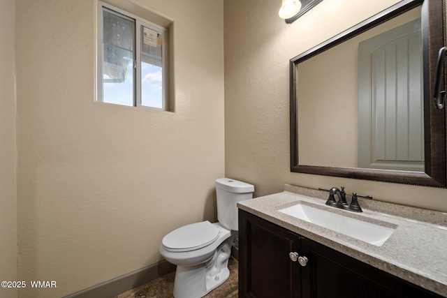 bathroom featuring baseboards, a textured wall, vanity, and toilet