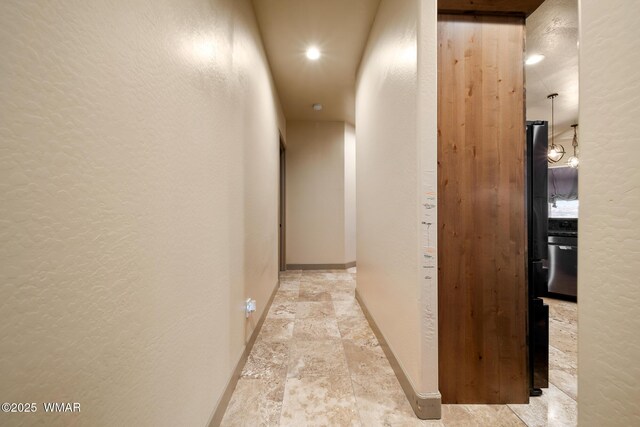 hall with stone finish flooring, a textured wall, and baseboards