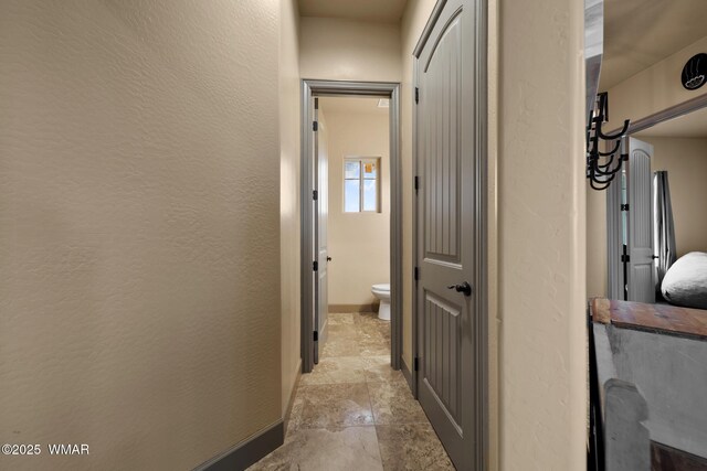 corridor featuring a textured wall, stone finish flooring, and baseboards