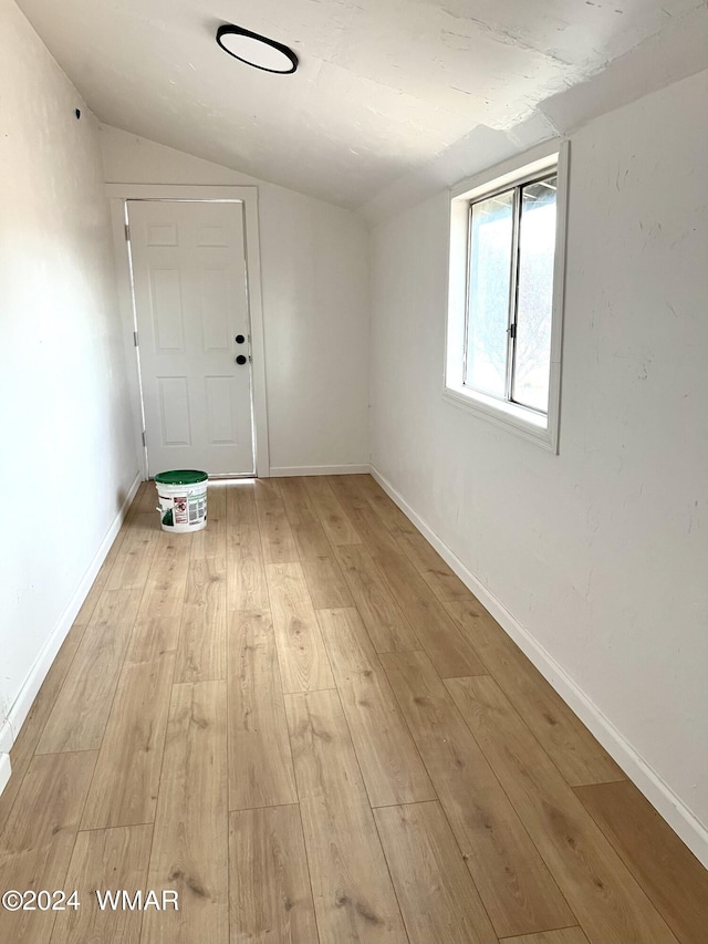 unfurnished room with light wood finished floors, baseboards, and vaulted ceiling