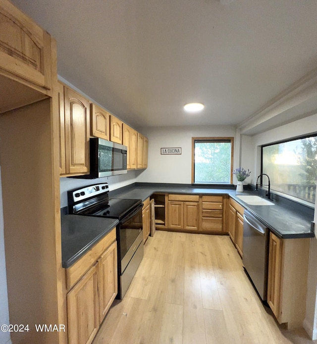 kitchen featuring appliances with stainless steel finishes, dark countertops, a sink, and light wood-style floors