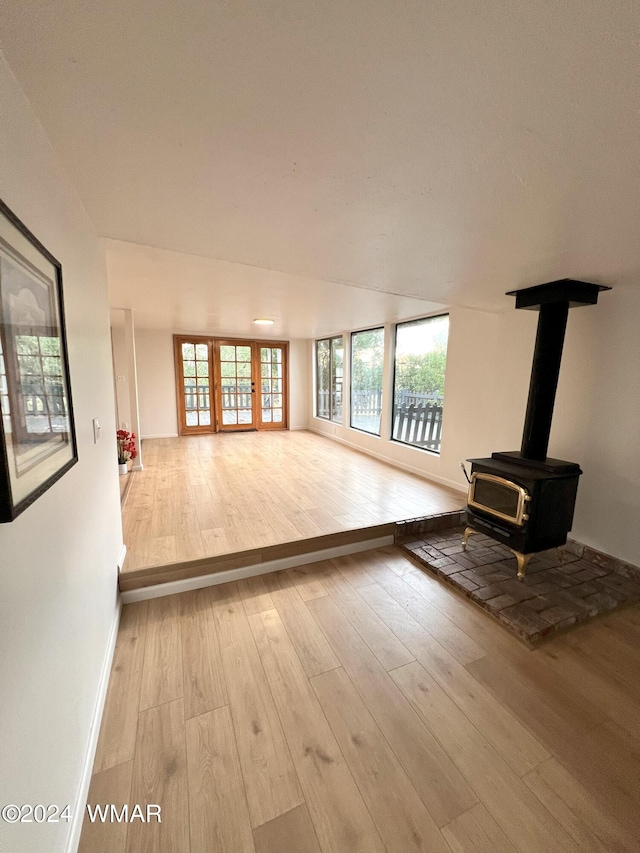 unfurnished living room featuring a wood stove, baseboards, and wood finished floors