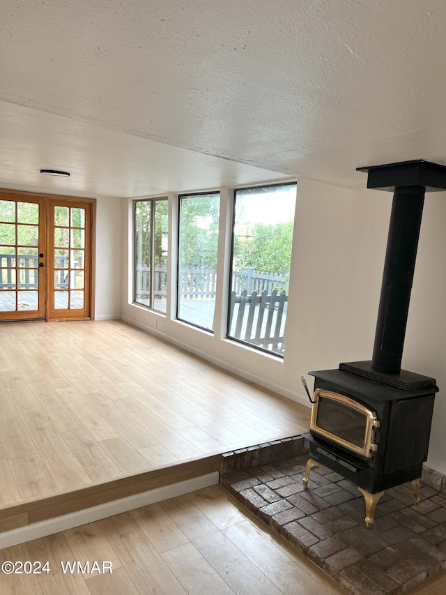 living room with a wood stove, light wood finished floors, baseboards, and a textured ceiling