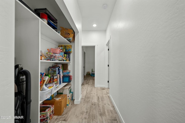 hallway featuring light wood-style floors, baseboards, and a textured wall