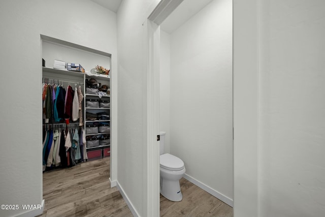 bathroom featuring a spacious closet, wood finished floors, toilet, and baseboards