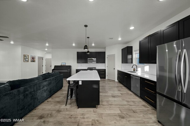 kitchen featuring stainless steel appliances, a sink, a kitchen island, open floor plan, and light countertops