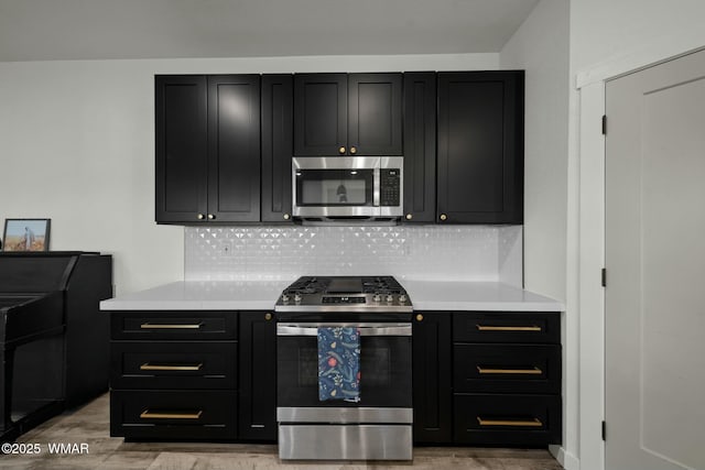 kitchen featuring stainless steel appliances, dark cabinetry, backsplash, and light countertops