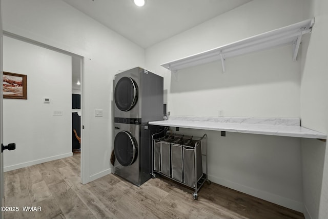 clothes washing area featuring stacked washer and dryer, baseboards, laundry area, and light wood-style floors