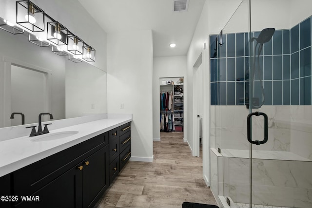 bathroom with wood finished floors, vanity, visible vents, a stall shower, and a walk in closet