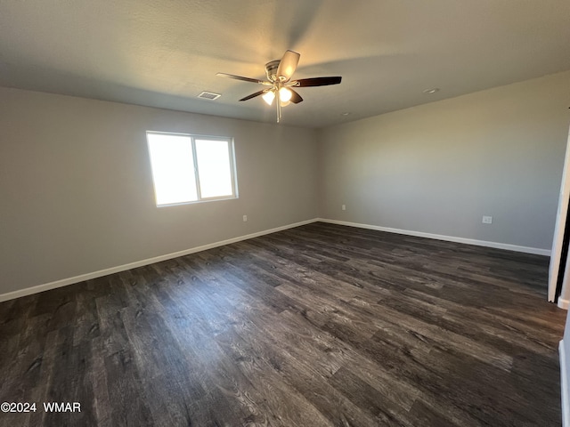 spare room with dark wood-type flooring, a ceiling fan, visible vents, and baseboards