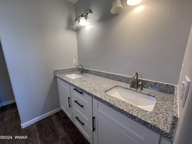 full bath with double vanity, wood finished floors, a sink, and baseboards