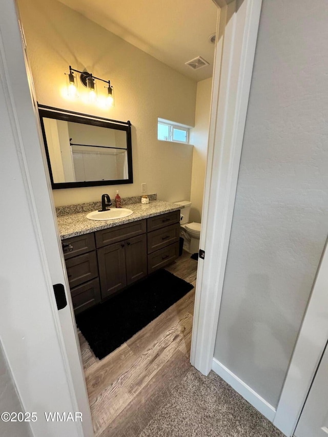 bathroom featuring vanity, wood finished floors, baseboards, visible vents, and toilet